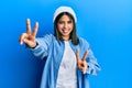 Young latin woman wearing cute wool cap smiling with tongue out showing fingers of both hands doing victory sign Royalty Free Stock Photo