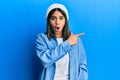 Young latin woman wearing cute wool cap surprised pointing with finger to the side, open mouth amazed expression Royalty Free Stock Photo