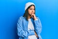 Young latin woman wearing cute wool cap thinking worried about a question, concerned and nervous with hand on chin