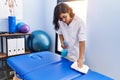 Young latin woman wearing physiotherapist uniform cleaning massage table at physiotherapy clinic Royalty Free Stock Photo