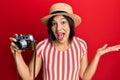 Young latin woman wearing summer hat holding vintage camera celebrating achievement with happy smile and winner expression with Royalty Free Stock Photo