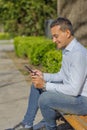 Young Latino man making a purchase with a credit card on his mobile phone sitting on a bench Royalty Free Stock Photo