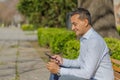 Young Latino man making a purchase with a credit card on his mobile phone sitting on a bench in a public park Royalty Free Stock Photo