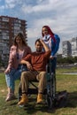 Young Latino paraplegic in a wheelchair in a park two young Caucasian girls