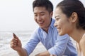 Young laughing couple looking at seashell at the waters edge, China Royalty Free Stock Photo