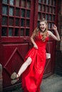 Young laughing girl with blond flowing long hair and beautiful make-up, in a long red dress, jumps along the street Royalty Free Stock Photo