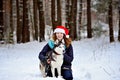 Young laughing girl in a Christmas hat with a Husky dog in the winter forest. She sits and hugs her dog. She looks into Royalty Free Stock Photo