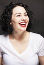 Young laughing girl in a white T-shirt on a black background. Bright brunette with curly hair. Close-up. Royalty Free Stock Photo