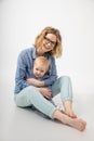 Young laughing woman mother holding embracing little blond blue-eyed girl baby daughter, covering with shirt, posing.