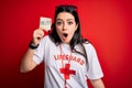 Young lifeguard woman holding paper note with help word over red background scared in shock with a surprise face, afraid and