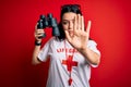 Young lifeguard woman wearing secury guard equipent holding binoculars over red background with open hand doing stop sign with