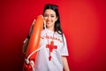 Young lifeguard woman wearing secury guard equipent holding rescue float over red background with a happy face standing and