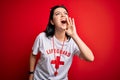 Young lifeguard woman wearing secury guard equipent over red background shouting and screaming loud to side with hand on mouth