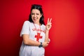 Young lifeguard woman wearing secury guard equipent over red background smiling with happy face winking at the camera doing