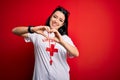 Young lifeguard woman wearing secury guard equipent over red background smiling in love doing heart symbol shape with hands