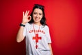 Young lifeguard woman wearing secury guard equipent over red background smiling positive doing ok sign with hand and fingers