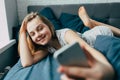 Young light brown hair woman in bed at home. Happy  girl smiling having  video call  on mobile telephone.  Teenager lying in bed a Royalty Free Stock Photo