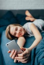 Young light brown hair woman in bed at home. Happy  girl smiling while texting message on mobile telephone.  Teenager lying in bed Royalty Free Stock Photo