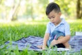 Young little asian boy reading and writing book in the park, asia kid homework and study in the summer, child relax with drawing Royalty Free Stock Photo