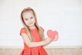 Young little blonde girl wearing in long sleeveless dress holding red cardboard heart Royalty Free Stock Photo