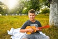 Young little boy guitarist outdoor. Boy on city park summer meadow enjoying day playing guitar Royalty Free Stock Photo