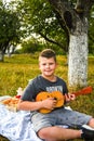 Young little boy guitarist outdoor. Boy on city park summer meadow enjoying day playing guitar Royalty Free Stock Photo