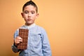 Young little boy kid eating sweet chocolate bar for dessert over isolated yellow background with a confident expression on smart Royalty Free Stock Photo