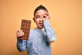 Young little boy kid eating sweet chocolate bar for dessert over isolated yellow background with happy face smiling doing ok sign Royalty Free Stock Photo