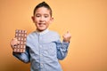 Young little boy kid eating sweet chocolate bar for dessert over isolated yellow background screaming proud and celebrating Royalty Free Stock Photo