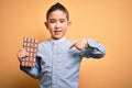 Young little boy kid eating sweet chocolate bar for dessert over isolated yellow background with surprise face pointing finger to Royalty Free Stock Photo