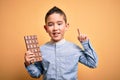 Young little boy kid eating sweet chocolate bar for dessert over isolated yellow background surprised with an idea or question Royalty Free Stock Photo