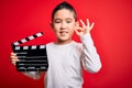 Young little boy kid filming video holding cinema director clapboard over isolated red background doing ok sign with fingers,