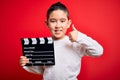 Young little boy kid filming video holding cinema director clapboard over isolated red background happy with big smile doing ok