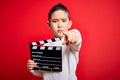 Young little boy kid filming video holding cinema director clapboard over isolated red background pointing with finger to the