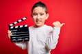 Young little boy kid filming video holding cinema director clapboard over isolated red background pointing and showing with thumb