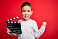 Young little boy kid filming video holding cinema director clapboard over isolated red background screaming proud and celebrating