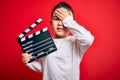 Young little boy kid filming video holding cinema director clapboard over isolated red background stressed with hand on head,