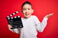 Young little boy kid filming video holding cinema director clapboard over isolated red background very happy and excited, winner