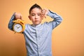 Young little boy kid holding classic bell alarm clock over isolated yellow background with angry face, negative sign showing Royalty Free Stock Photo