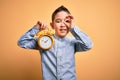 Young little boy kid holding classic bell alarm clock over isolated yellow background with happy face smiling doing ok sign with Royalty Free Stock Photo