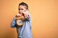 Young little boy kid holding classic bell alarm clock over isolated yellow background pointing with finger to the camera and to Royalty Free Stock Photo