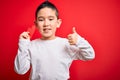 Young little boy kid holding heart paper shape over isolated red background happy with big smile doing ok sign, thumb up with Royalty Free Stock Photo