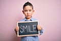 Young little boy kid showing blackboard with smile word as happy message over pink background with a confident expression on smart Royalty Free Stock Photo