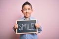 Young little boy kid showing blackboard with smile word as happy message over pink background with a happy face standing and Royalty Free Stock Photo