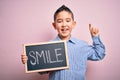 Young little boy kid showing blackboard with smile word as happy message over pink background surprised with an idea or question Royalty Free Stock Photo