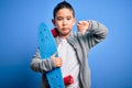 Young little boy kid skateboarder holding modern skateboard over blue isolated background with angry face, negative sign showing Royalty Free Stock Photo