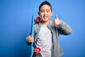 Young little boy kid skateboarder holding modern skateboard over blue isolated background happy with big smile doing ok sign, Royalty Free Stock Photo