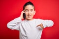 Young little boy kid talking on smartphone mobile over red isolated background with surprise face pointing finger to himself Royalty Free Stock Photo