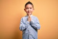 Young little boy kid wearing elegant shirt standing over yellow isolated background praying with hands together asking for Royalty Free Stock Photo