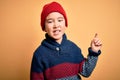 Young little boy kid wearing wool cap and winter sweater over yellow isolated background with a big smile on face, pointing with Royalty Free Stock Photo
